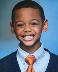A young boy in a blue shirt and orange tie smiles for the camera.