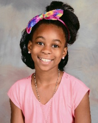 A young girl in a pink shirt with a bow on her head.