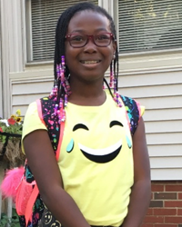 A young girl wearing a smiley face backpack.