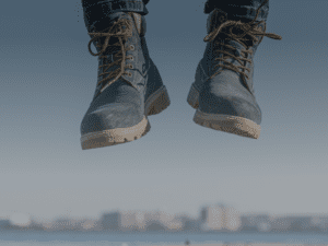 A person, embodying the essence of bootstrapping, is captured mid-jump in blue jeans and green boots with a blurred cityscape in the background.