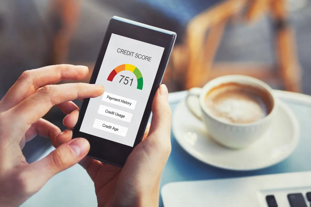 A person holds a smartphone displaying a credit score of 751 and categories for payment history, credit usage, and credit age—highlighting their Financial Love Language—with a cup of coffee and saucer on the table in the background.