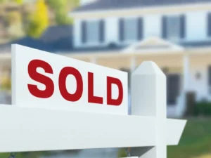 A "Sold" sign in front of a blurred image of a house emphasizes the impact of current mortgage rates.