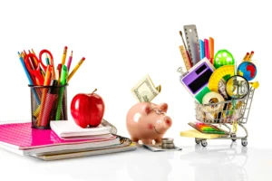 A collection of school supplies including notebooks, pens, and an apple on the left, with a piggy bank, money, and a small shopping cart filled with more supplies on the right, on a white background.