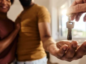 A couple happily receives house keys from another person, symbolizing their dream purchase with first-time homebuyer assistance.