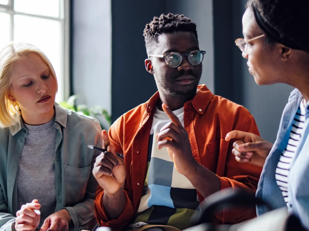 A trio settles into conversation about retirement plans, with one thoughtfully holding a pen.