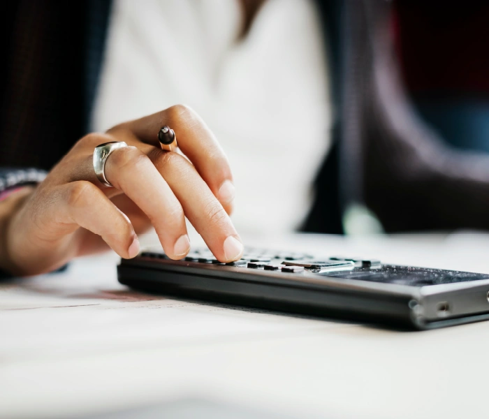 A person is using a calculator, pressing buttons with one hand while holding a pencil in the other.