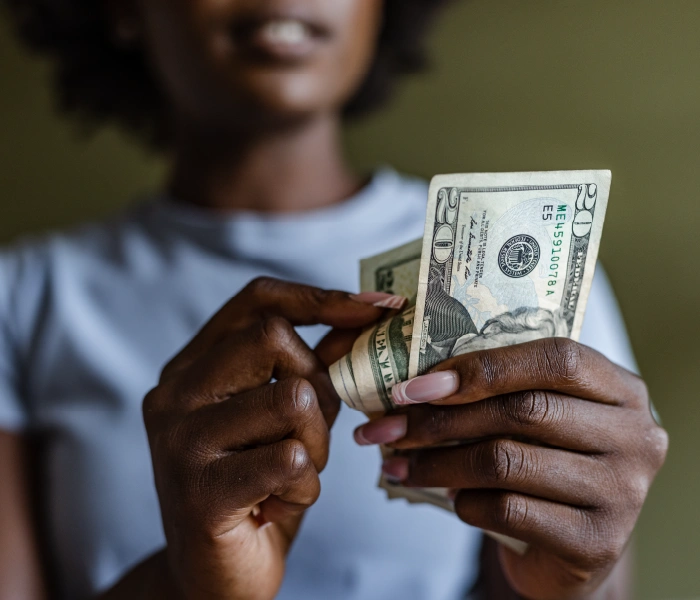 A person in a gray shirt holds and counts a stack of U.S. twenty-dollar bills.