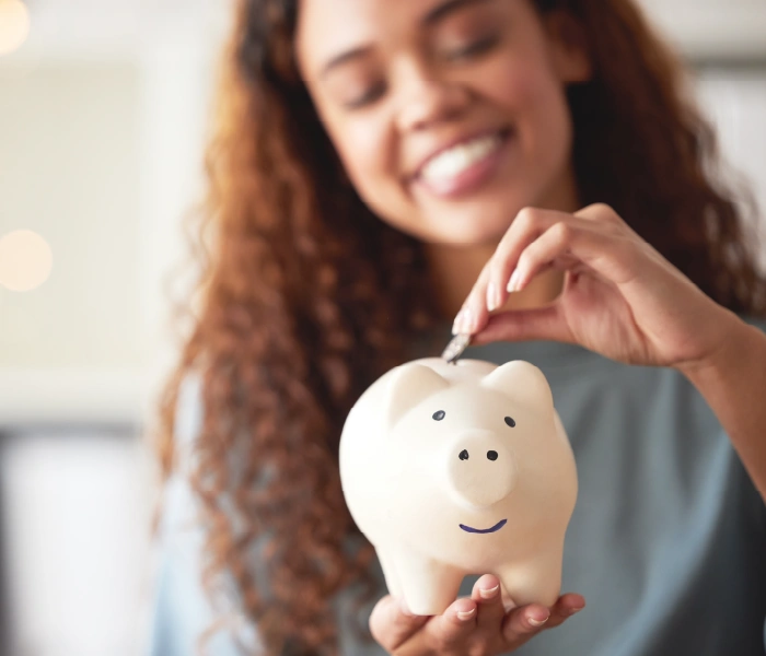 A person smiles while placing a coin into a white piggy bank.