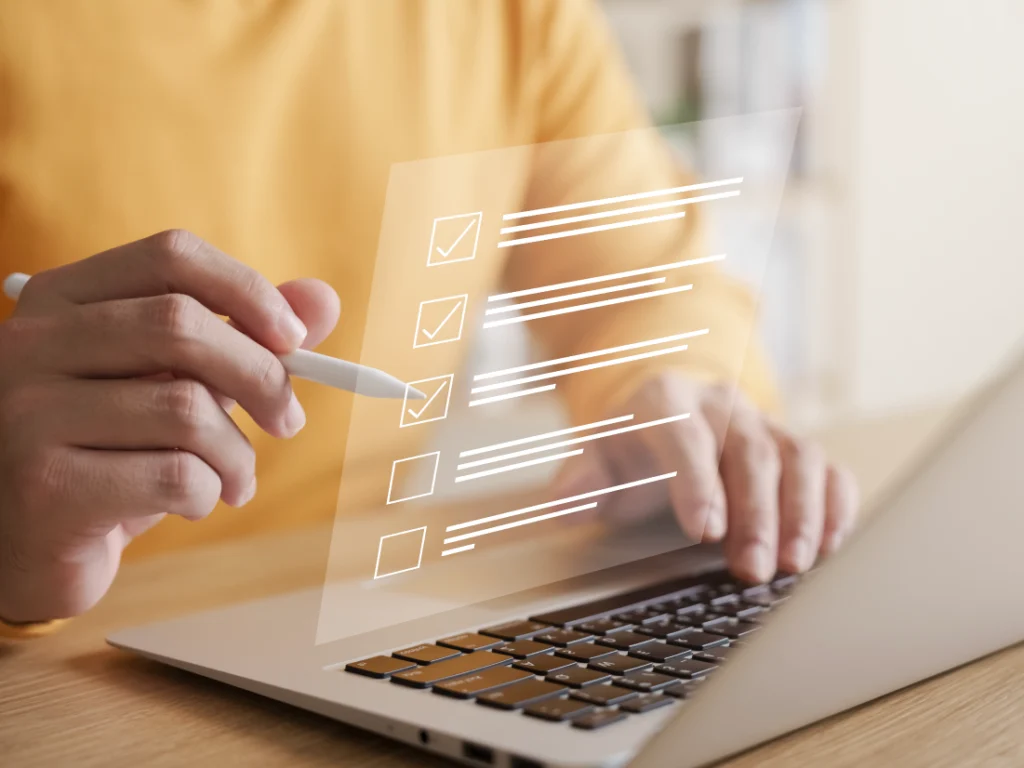 A person uses a stylus to interact with a Financial Detox checklist graphic displayed above a laptop keyboard.