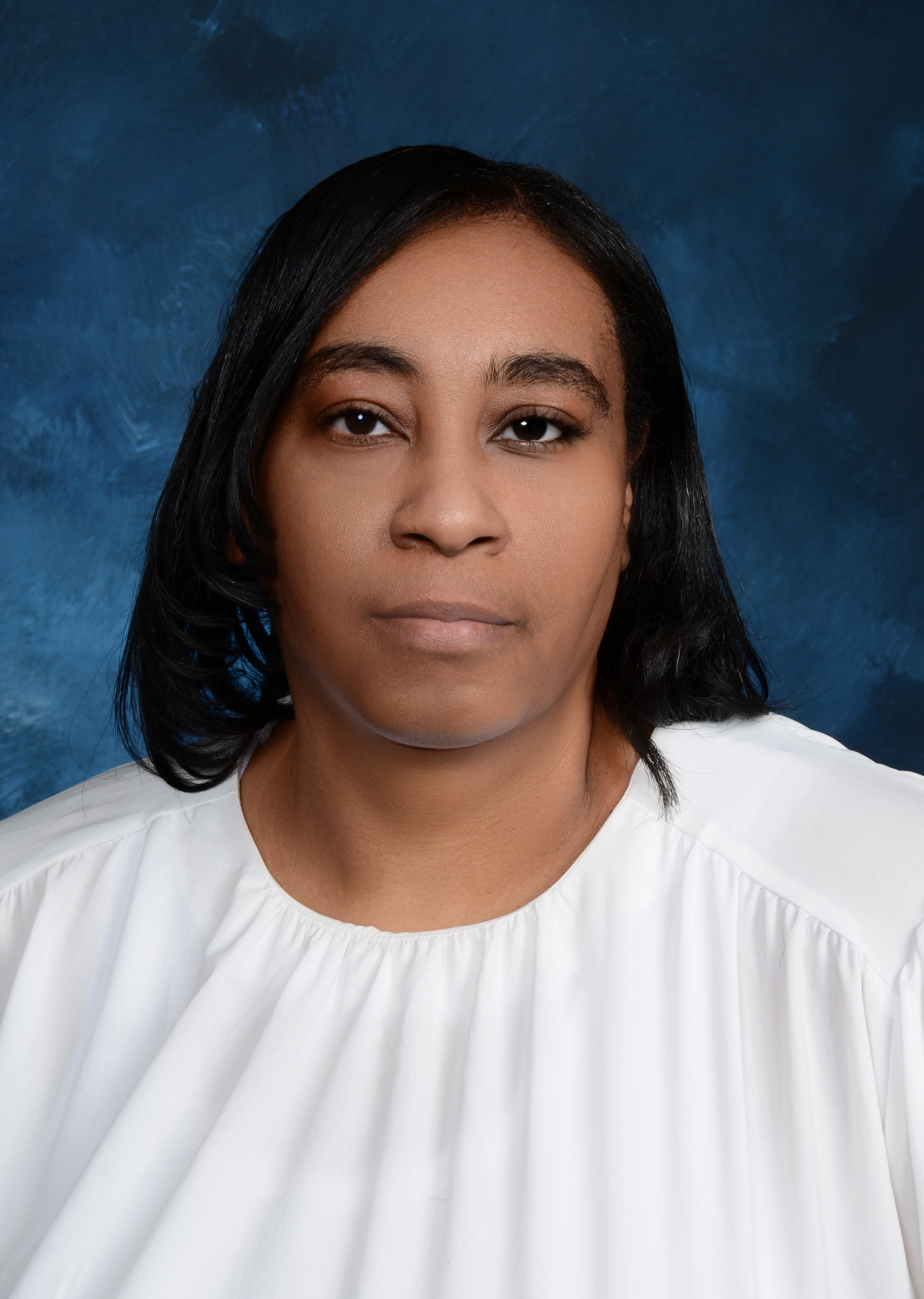 Portrait of a person with long dark hair wearing a white top against a dark blue background.