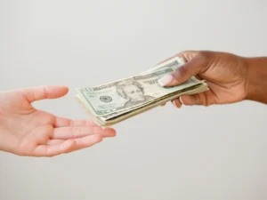 One person handing a stack of US dollar bills to another, subtly highlighting potential tax benefits against a neutral background.